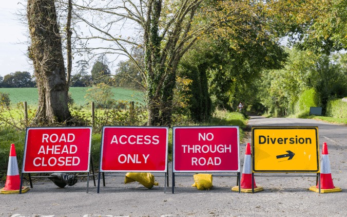 Road closure signs displayed on a rural road, including 'Road Ahead Closed,' 'Access Only,' 'No Through Road,' and 'Diversion' with directional arrow, highlighting traffic management measures. The road closure has been approved as a temporary traffic regulation order which will soon be required to comply with Digital Traffic Regulation Order requirements. 