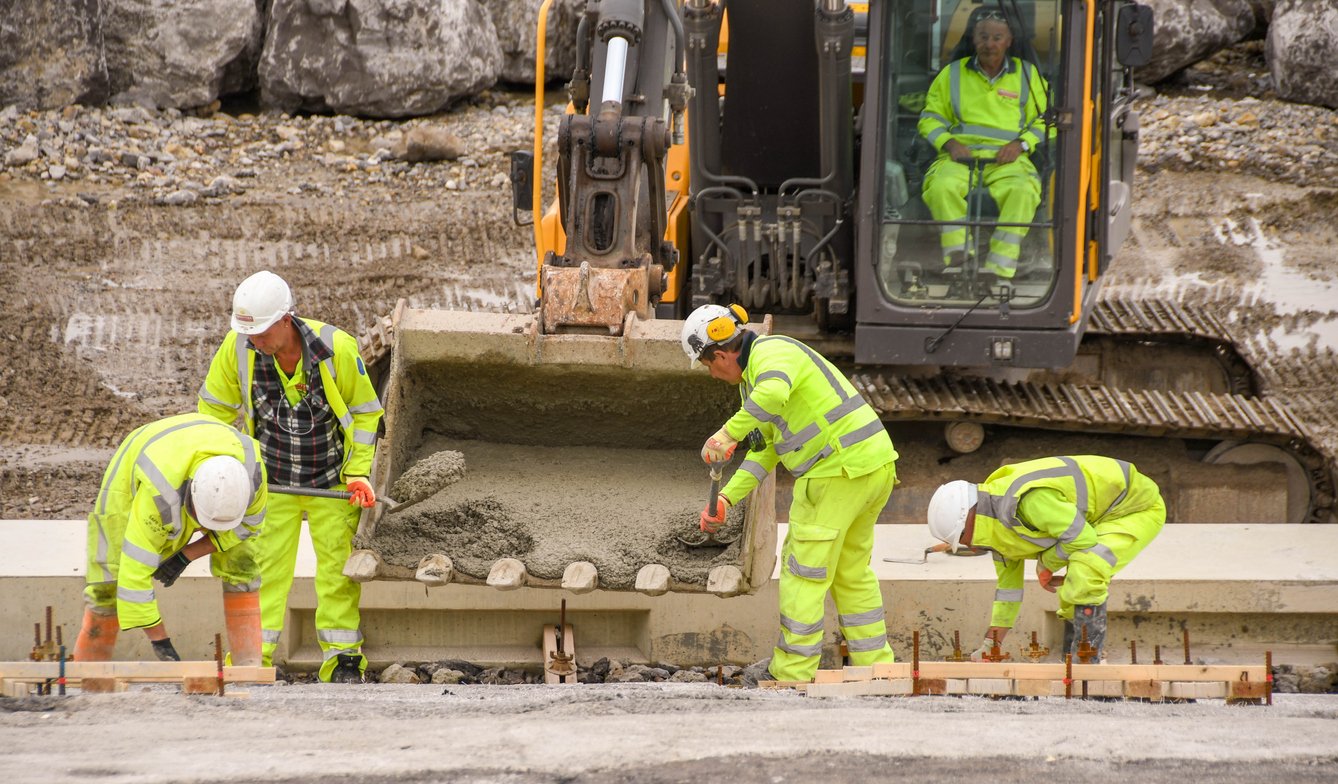 Three construction workers scoop sand from a digger on a construction site