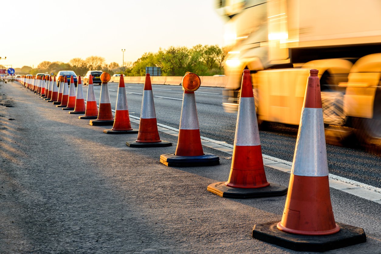 Highway maintenance cones are spread across the road while construction crews work